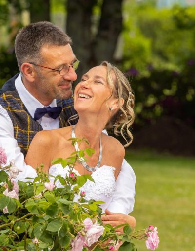 Portrait de mariés complices et joyeux près d'un buisson de roses, photographe mariage Orléans champêtre